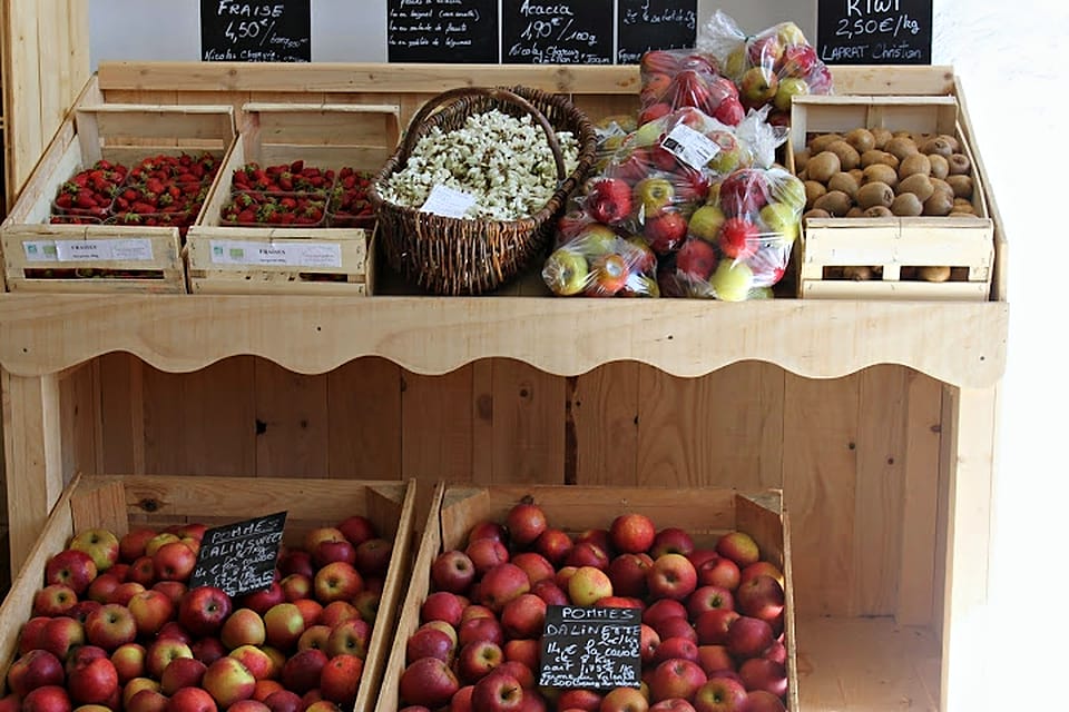 L'étal des fruits du magasin : fraises en barquettes, pommes en sachets et en cagettes, kiwis, sous les ardoises