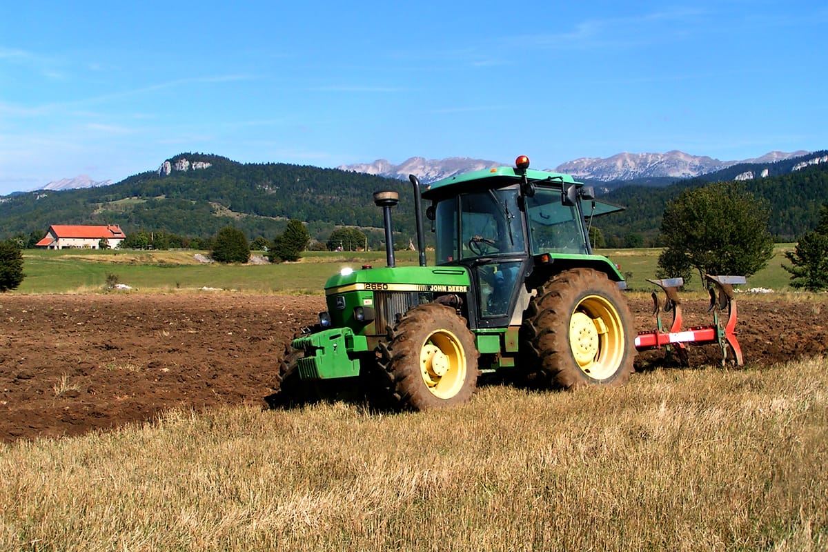 Un tracteur laboure un champ du plateau de Vassieux, devant les falaises du Vercors