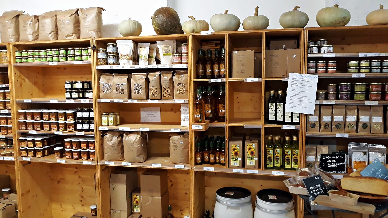 Les étagères en bois du magasin : bocaux, farines, huiles, et des courges de saison posées en haut